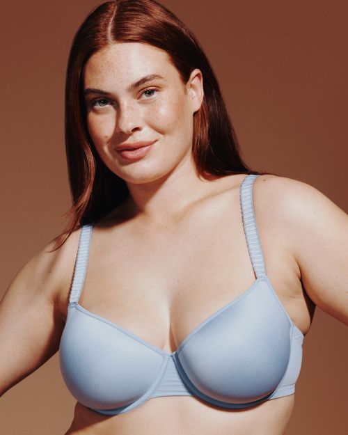 Close-up of a woman with red hair wearing a light blue bra against a neutral background. Beauty and fashion photography.