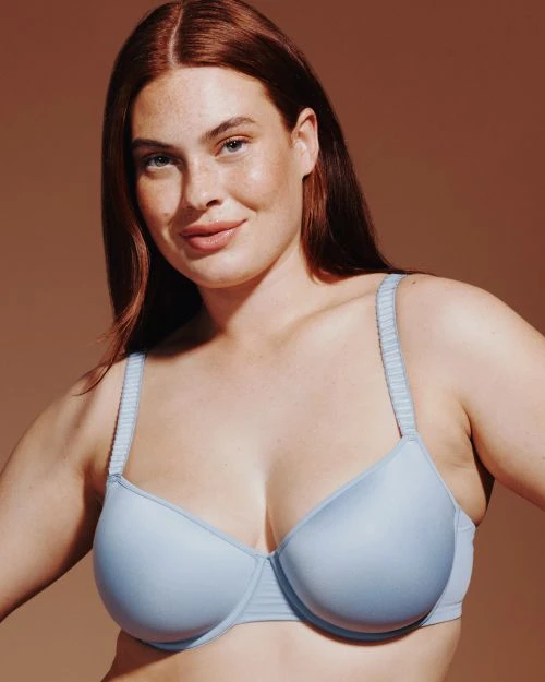 Close-up of a woman with red hair wearing a light blue bra against a neutral background. Beauty and fashion photography.