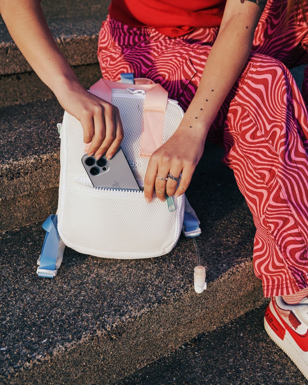 Person holding a white mesh backpack with a visible cell phone in the front pocket, showcasing a casual and youthful style.
