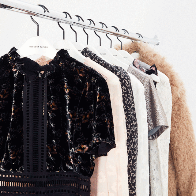 Several women's dresses hang on a metal rack in a clothing store, featuring various fabrics, patterns, and styles.