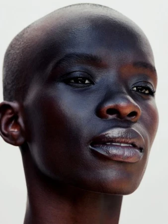 Close-up portrait of a bald Black woman with a serious expression against a plain white background shot by Katie Thompson.