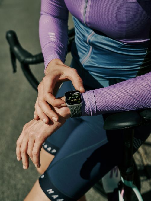 Close-up of a woman checking her smartwatch while resting her arms on a bicycle during a cycling activity outdoors.