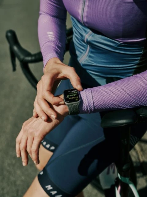 Close-up of a woman checking her smartwatch while resting her arms on a bicycle during a cycling activity outdoors.