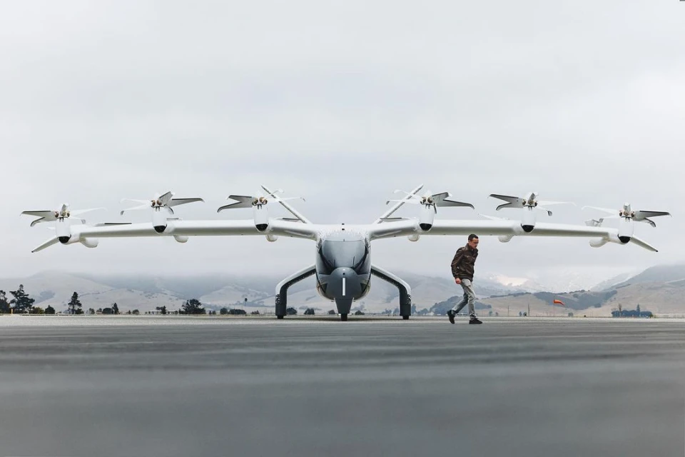 Wide shot of a futuristic aircraft prototype on a tarmac with a man walking past, highlighting innovation in transportation design and technology.