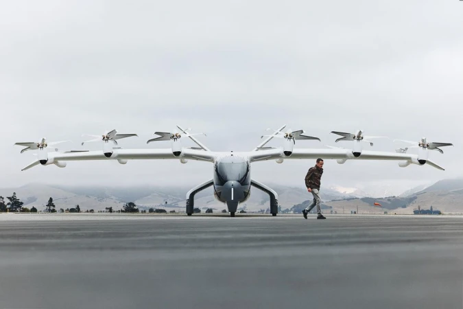 Wide shot of a futuristic aircraft prototype on a tarmac with a man walking past, highlighting innovation in transportation design and technology.
