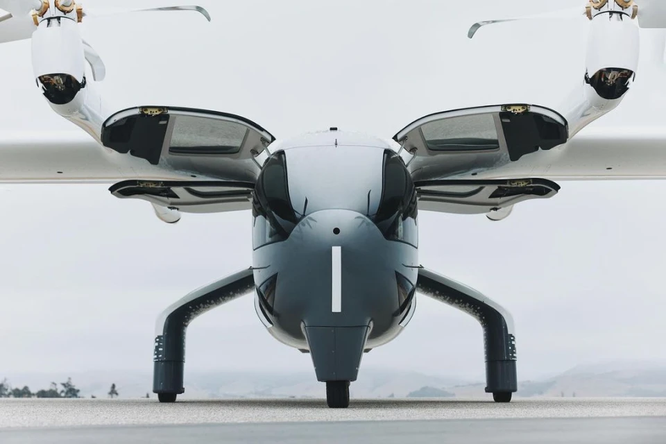 Front view of an electric vertical takeoff and landing (eVTOL) aircraft with rotors, landing gear, and sleek gray and white design.