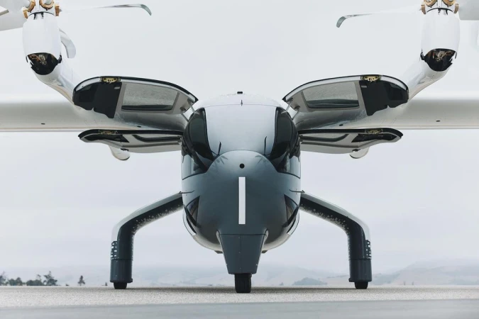 Front view of an electric vertical takeoff and landing (eVTOL) aircraft with rotors, landing gear, and sleek gray and white design.