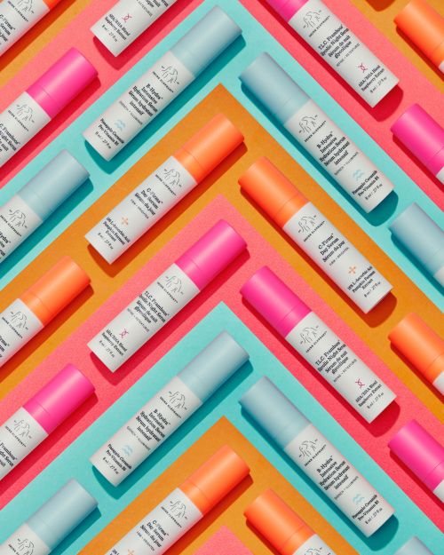 Multiple cosmetic tubes with blue, orange, and pink tops are arranged diagonally on a background of teal, orange, and pink.