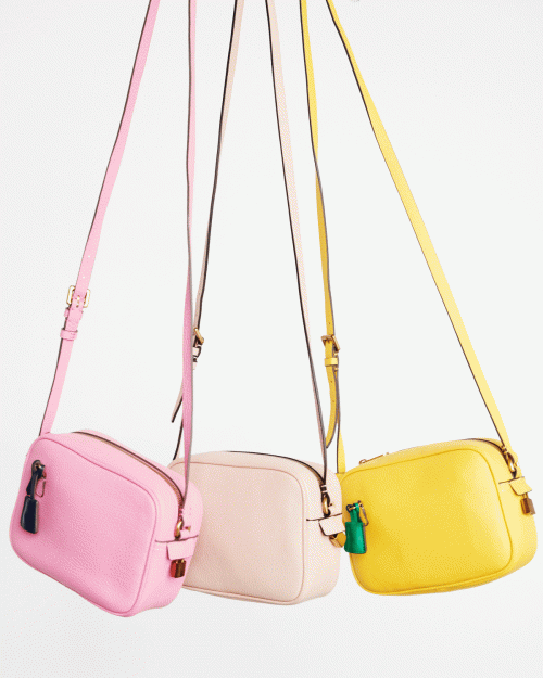 Three colorful leather crossbody bags hang against a white background. Pink, cream, and yellow purses display designer style and craftsmanship.