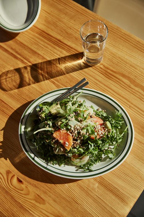 Close-up of a vibrant salad with citrus, greens, and seeds served on a plate with a glass of water on a wooden table.