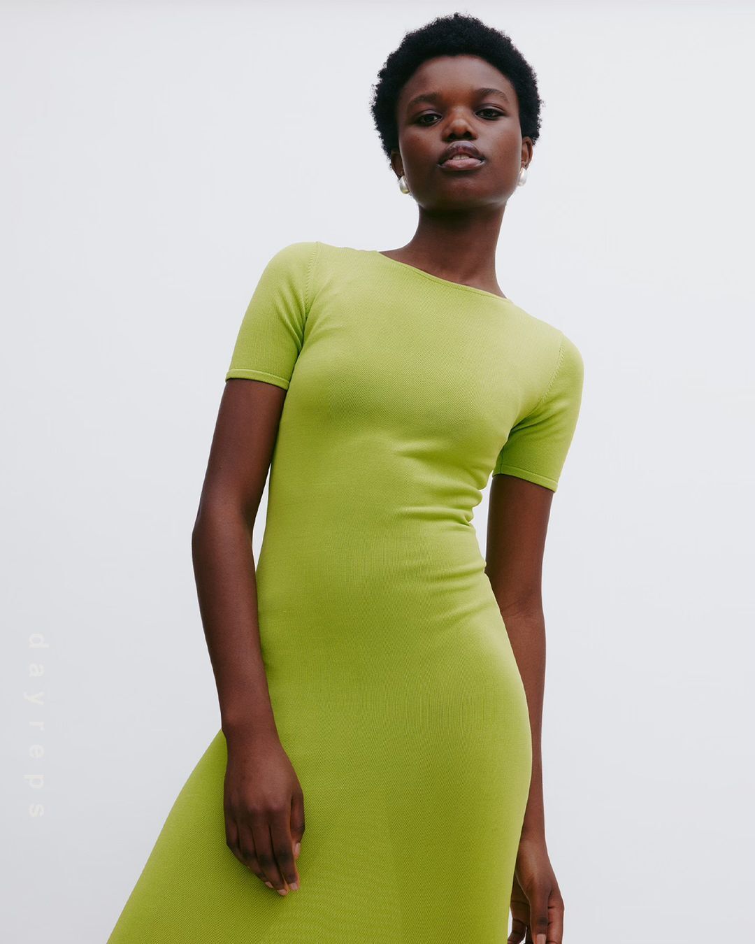 Adult woman poses in a full-length, bodycon, short-sleeve dress, with a light-grey background in a studio setting, focusing on fashion and style.