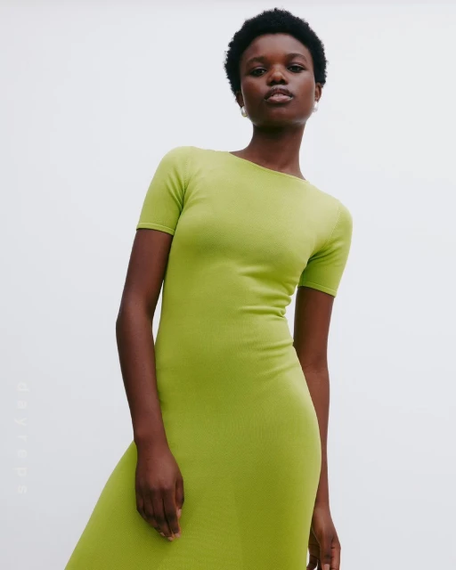 Adult woman poses in a full-length, bodycon, short-sleeve dress, with a light-grey background in a studio setting, focusing on fashion and style.