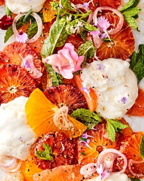 Overhead shot of a vibrant citrus salad with blood oranges, navel oranges, red onions, fresh herbs, and dollops of cream.