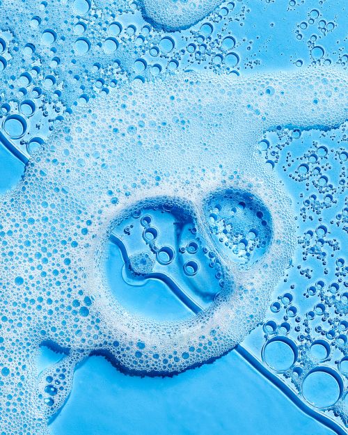 Close-up of light blue liquid with white soap bubbles and smaller bubbles for a clean, fresh, and textured beauty or cleaning product shot.
