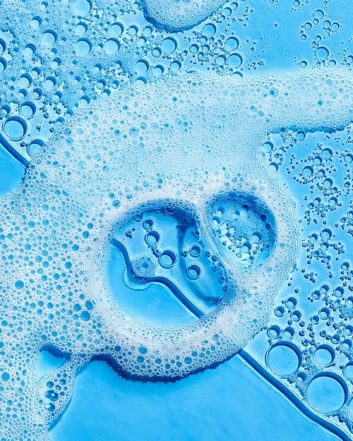 Close-up of light blue liquid with white soap bubbles and smaller bubbles for a clean, fresh, and textured beauty or cleaning product shot.