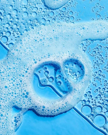 Close-up of light blue liquid with white soap bubbles and smaller bubbles for a clean, fresh, and textured beauty or cleaning product shot.