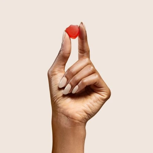 Close-up of a hand holding a red gummy vitamin against a neutral background, showcasing texture and color for wellness or food content.