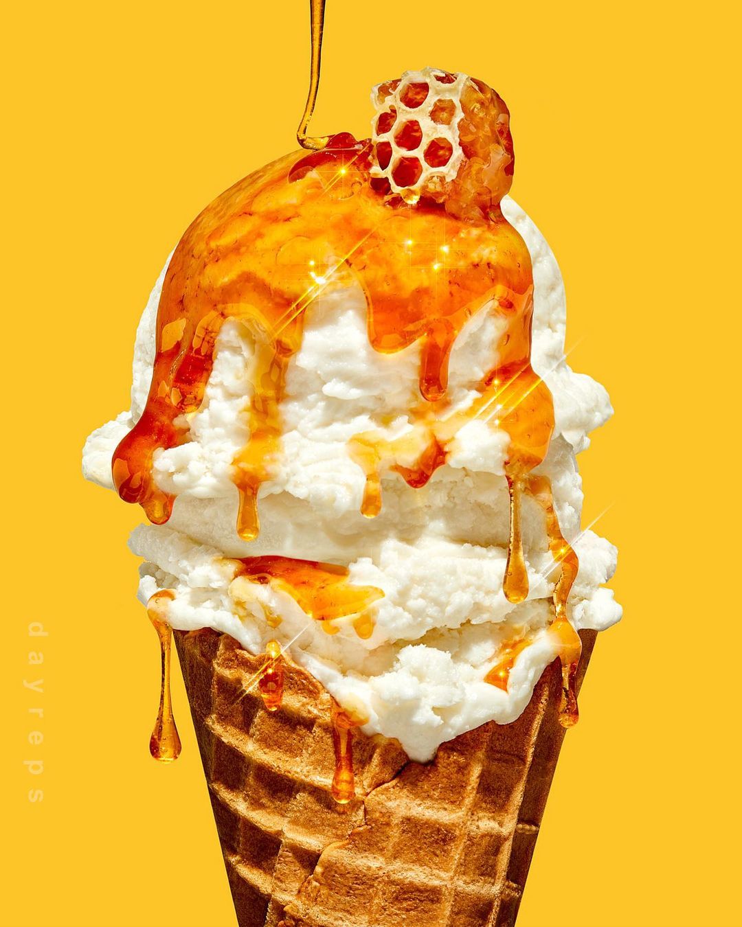 Close-up of a waffle cone filled with vanilla ice cream, drizzled with honey and topped with a piece of honeycomb on yellow.