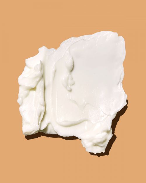 Close-up shot of a creamy white cosmetic product on a warm, neutral surface, highlighting its texture and color.