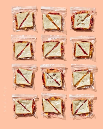 Eleven sealed plastic bags, each containing a diagonally-cut sandwich, arranged in rows against a light peach-colored background. Food photography.
