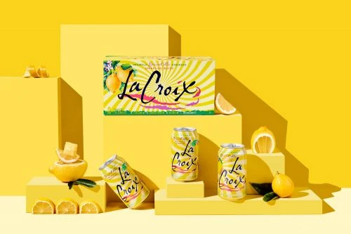 La Croix sparkling water cans and a carton are arranged on yellow platforms with lemons, creating a refreshing and vibrant food and beverage scene.
