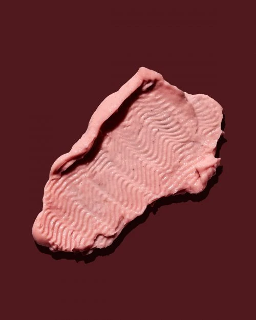 Close-up of a vibrant pink cosmetic cream swatch with a textured surface, set against a dark brown background, highlighting beauty and texture.