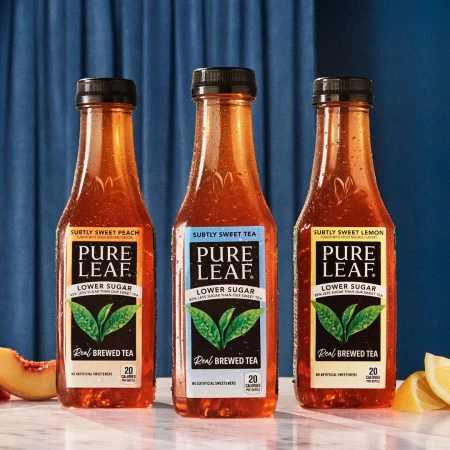Three bottles of Pure Leaf iced tea in peach, tea, and lemon flavors line a marble counter with peach and lemon slices on a navy background.