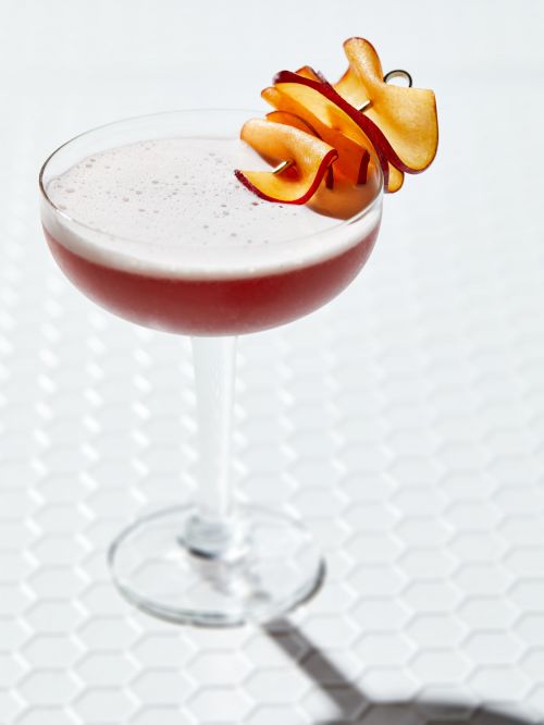 Elegant cocktail with apple garnish on a honeycomb-tiled surface, showcasing beverage photography for drinks and food styling.