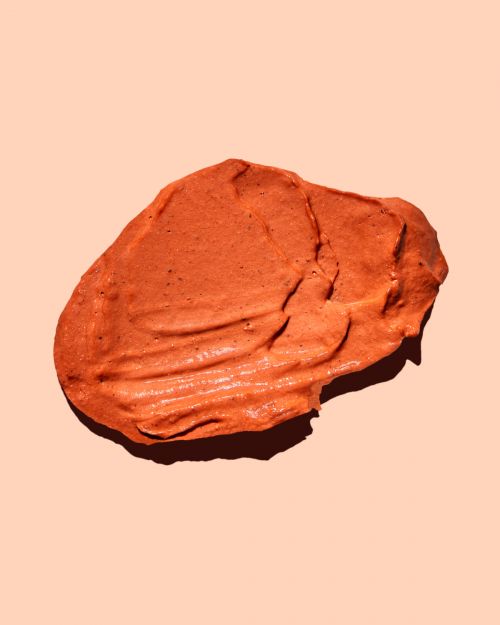 Textured orange beauty clay mask swipe on a peach background in a beauty product demonstration, studio lit, close-up shot.