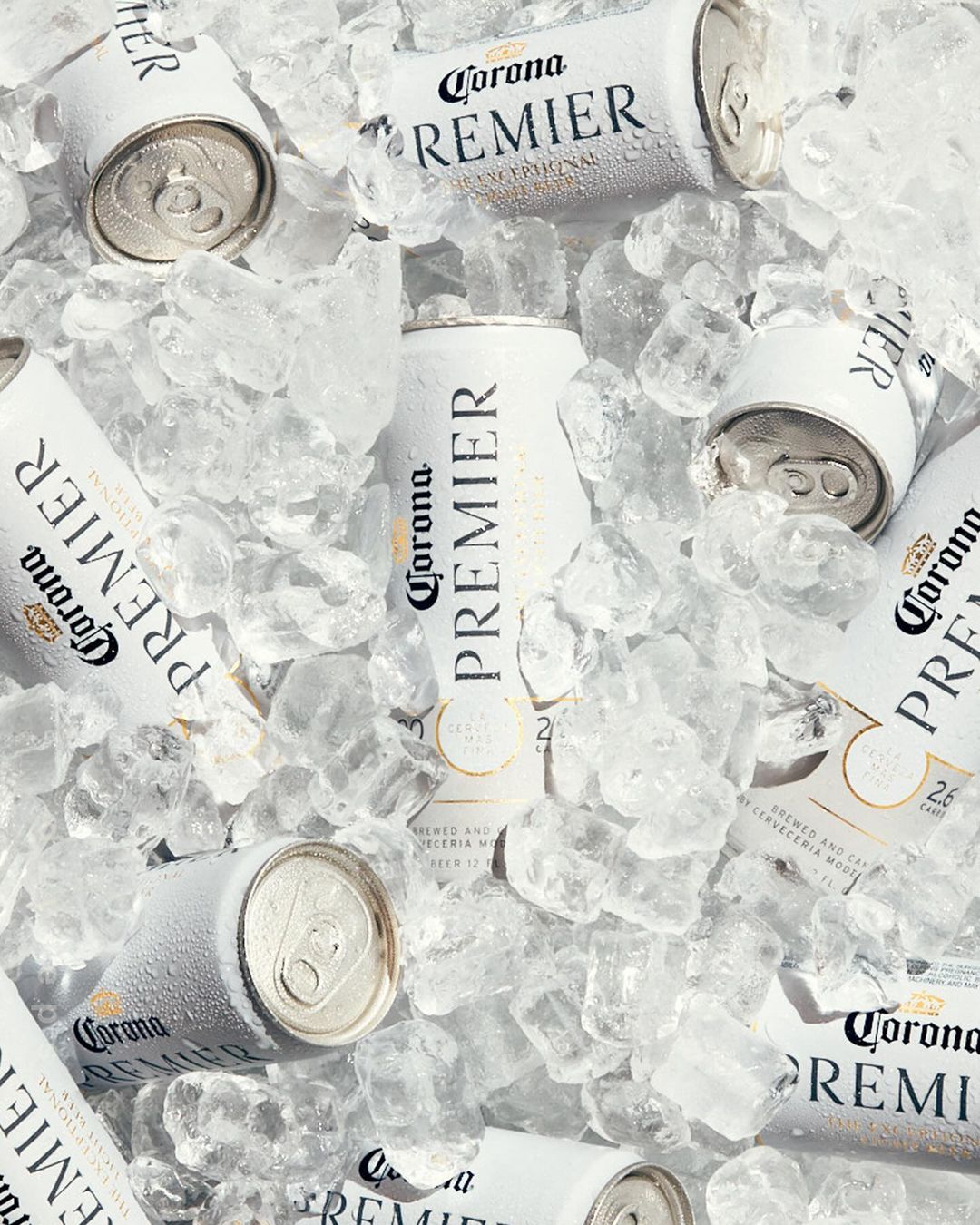Overhead shot of white Corona Premier beer cans nestled in crushed ice, creating a refreshing, cool beverage scene.