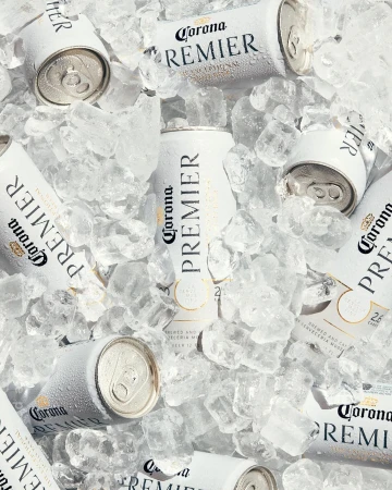 Overhead shot of white Corona Premier beer cans nestled in crushed ice, creating a refreshing, cool beverage scene.