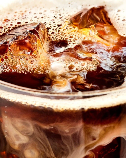 Close-up of iced coffee in a glass with ice cubes and cream swirling to create a textured, refreshing beverage drink.