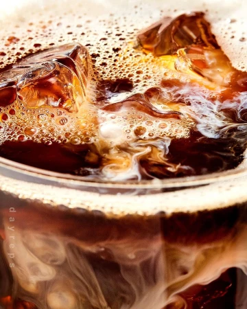 Close-up of iced coffee in a glass with ice cubes and cream swirling to create a textured, refreshing beverage drink.