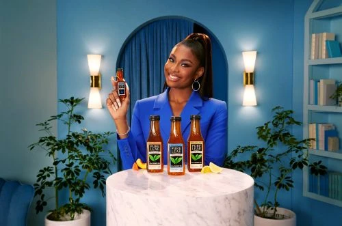 A smiling Black woman in a blue suit holds up a Pure Leaf Tea bottle; three more bottles sit on a marble table with citrus.
