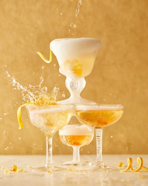 Champagne tower with fizzing drink, lemon peel garnish, and golden background for celebrations, parties, and upscale food and beverage concepts.