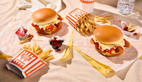Overhead shot of two chicken sandwiches with french fries and condiments arranged on a branded paper, featuring fast-food cuisine.