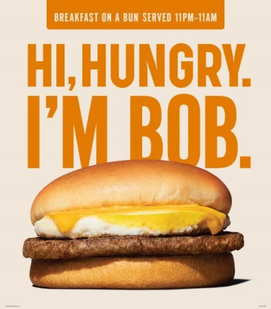 Close-up of a breakfast burger with egg and sausage between two buns on a beige background, next to orange text that reads, 'Hi, Hungry. I'm Bob.'
