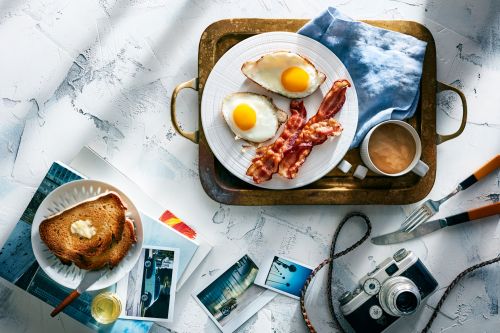 Overhead shot of breakfast featuring fried eggs, bacon, and toast on a tray, accompanied by coffee and a vintage camera for a nostalgic feel.