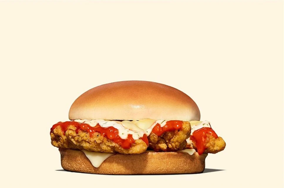 Delicious chicken sandwich with creamy white sauce and red sauce on a light yellow background in a close-up, appetizing food shot.