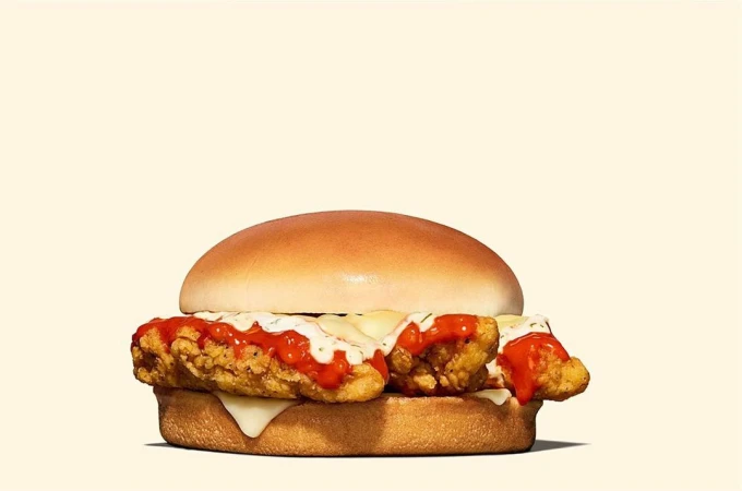 Delicious chicken sandwich with creamy white sauce and red sauce on a light yellow background in a close-up, appetizing food shot.
