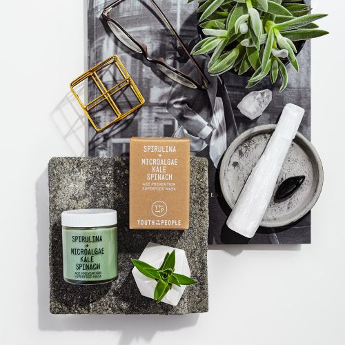 Still life product photography featuring Youth To The People skincare, succulents, crystals, and glasses on a white surface.