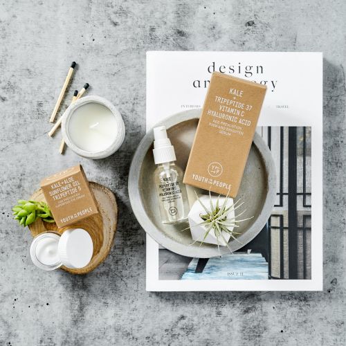 Overhead shot of Youth To The People skincare products: toner, cream, and gel, complemented by a magazine, matches, and decorative plants.