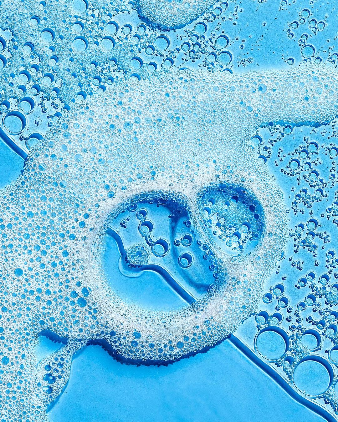 Close-up shot of translucent blue liquid with white foam bubbles on a flat surface, suitable for backgrounds in beauty and healthcare themes.