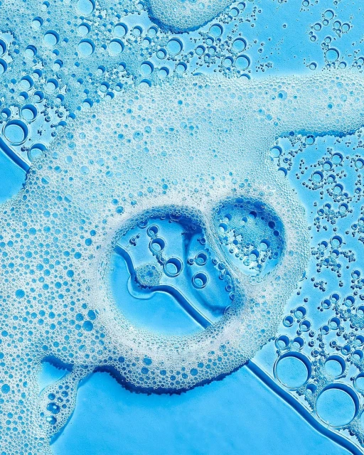 Close-up shot of translucent blue liquid with white foam bubbles on a flat surface, suitable for backgrounds in beauty and healthcare themes.