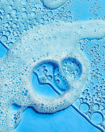 Close-up shot of translucent blue liquid with white foam bubbles on a flat surface, suitable for backgrounds in beauty and healthcare themes.