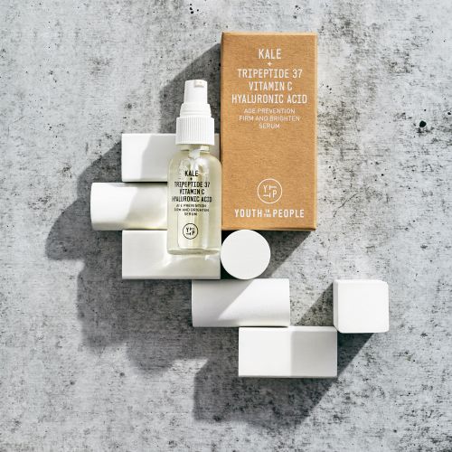 Product shot of Youth To The People skincare serum and box on white blocks against a gray textured background in eye-level, studio lighting.