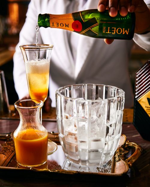 Close-up of a bartender pouring Moet champagne into a cocktail glass, featuring an ice bucket and various cocktail ingredients.