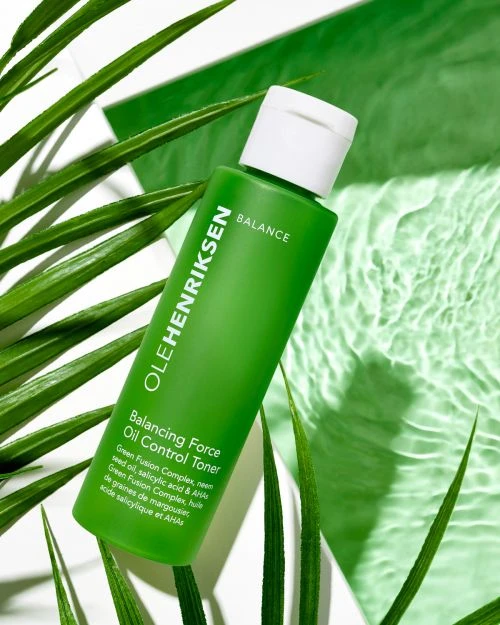 Ole Henriksen Balancing Force Oil Control Toner bottle with white cap, surrounded by green palm leaves and water ripple effects.