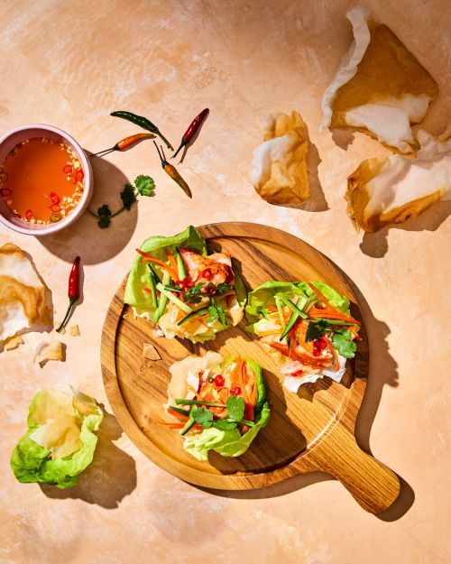 Overhead shot of three lettuce wraps with shrimp and vegetable filling, served on a round wooden board with dipping sauce.