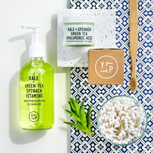 Flat lay of green tea cleanser, moisturizer, and bamboo toothbrush on patterned tile, promoting skincare and dental hygiene products.
